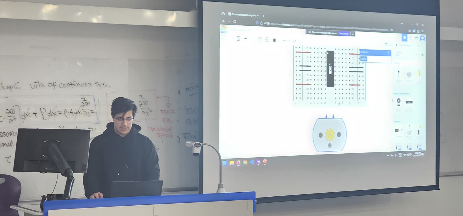 A workshop presenter at a laptop with a breadboard and motor simulation on the projector